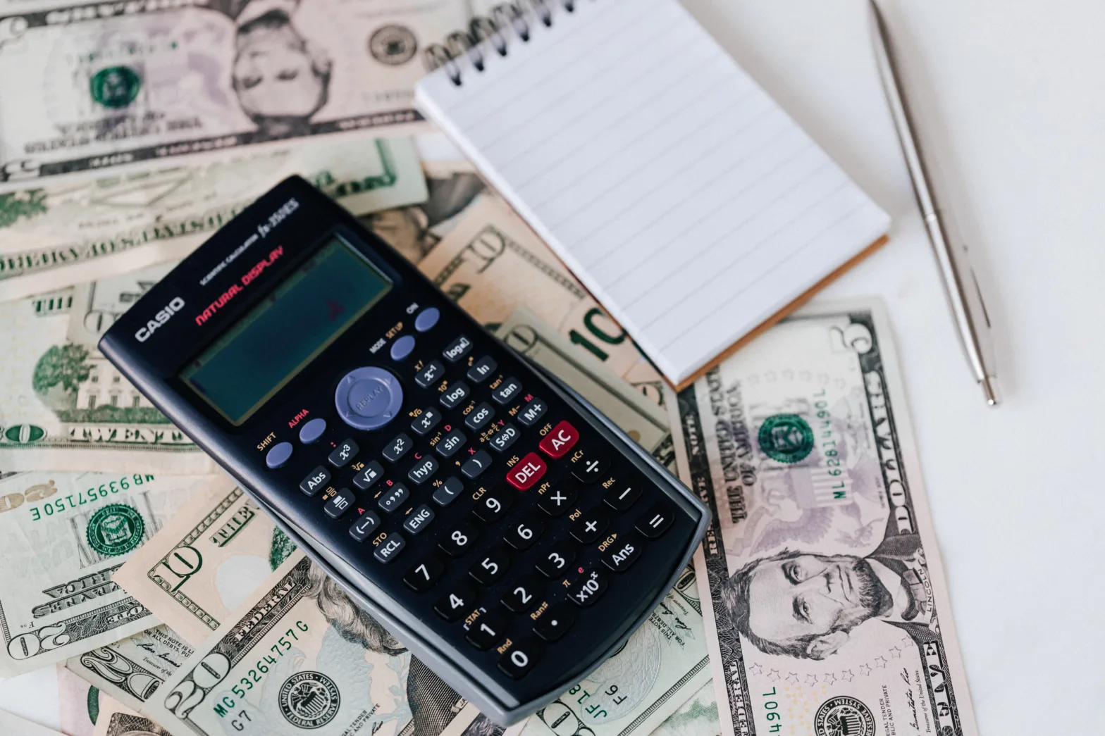 Calculator and notepad placed on USA dollars stack.